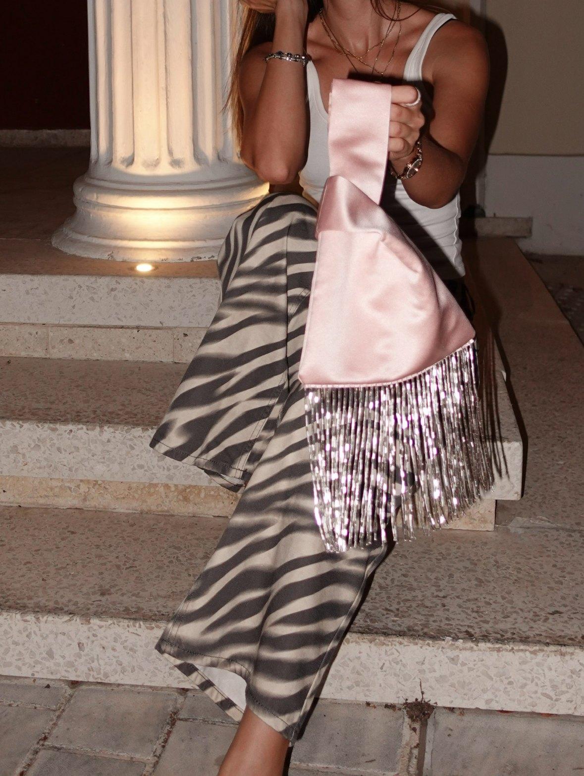 The Blush knot bag on marble steps after dark, its fringe catching the light
