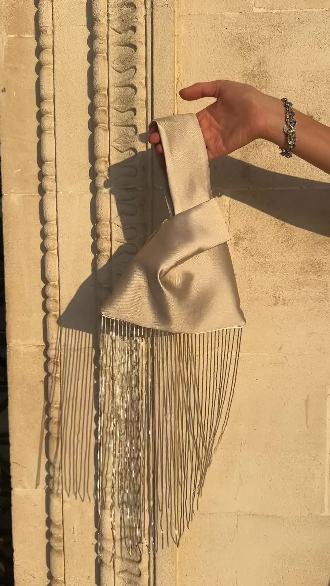 Champagne satin bag held against warm stone